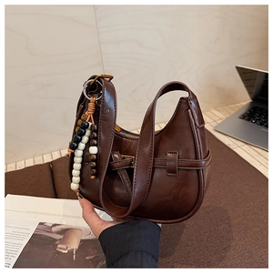 Close-up of brown vintage crescent bag featuring shiny leather texture and beaded tassel