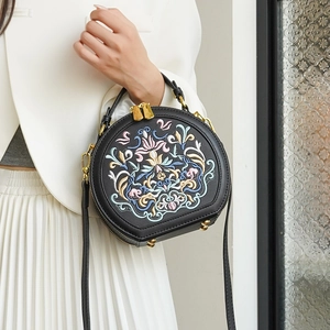 Detail shot of the embroidery and golden metal hardware on a black round crossbody bag