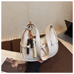 Detail of off-white hobo bag showing metallic buckle and wooden bead tassel charm
