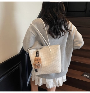 Detailed texture of white woven tote bag with a brown plush bear charm and pearl chain