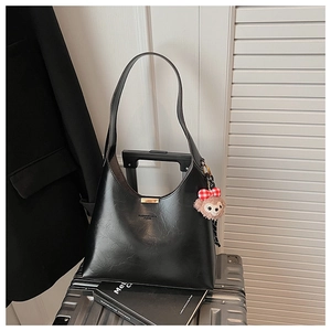 Detail of black faux leather hobo bag with gold metal trim and brown plush bear charm