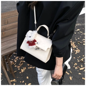 Detail of cream white leather handbag with silver twist lock and cute teddy bear charm