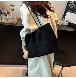Minimalist black suede tote bag with slim straps worn by model in a modern studio