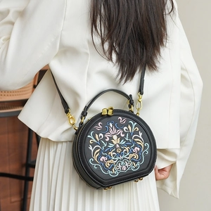 Detailed embroidery on a black circular crossbody bag styled with a minimalist white outfit