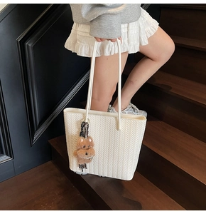 Detailed shot of beige woven tote bag with brown plush bear charm on wooden stairs