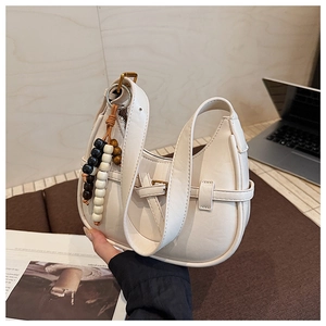 Detail of a beige moon-shaped hobo bag with a decorative beaded charm and smooth texture
