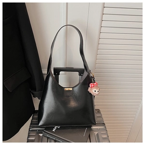 Detail of black textured PU leather bucket bag with cute plush bear charm on a suitcase