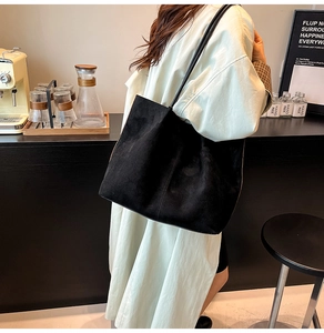 Detail of a large black suede tote bag shown in a stylish cafe setting for daily wear