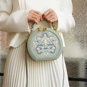Detail of sage green round crossbody bag with traditional floral embroidery and gold zipper
