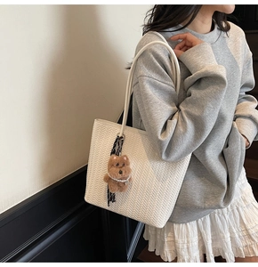 Detail of white woven tote bag with brown plush bear charm on long shoulder strap