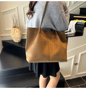 Detail of a large brown suede tote bag featuring slim shoulder straps and high capacity