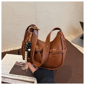 Detailed close-up of brown faux leather hobo bag with unique beaded charm and strap buckle