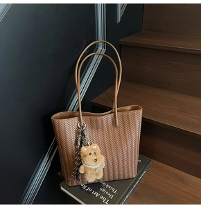 Detail of a brown woven leather tote bag with a small bear charm and stylish silk scarf