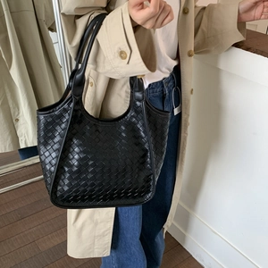 Detailed close-up of a large black woven leather tote bag with sturdy double handles