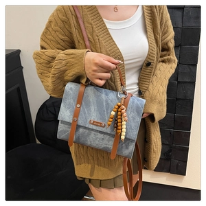 Détail d'un sac à dos en denim bleu avec lanières de cuir brun et pendentif en bois rétro