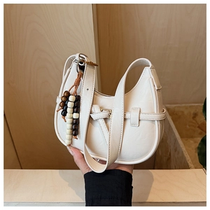 Detail of minimalist cream half-moon bag with decorative wooden beads and buckle