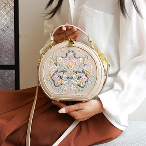 Close-up of intricate floral embroidery and gold zipper detail on the beige round bag