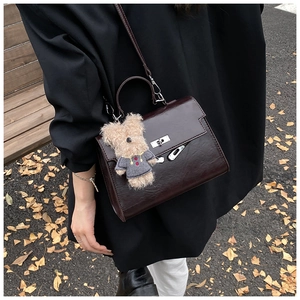 Detailed view of coffee brown leather Kelly-style bag with silver buckle and bear charm