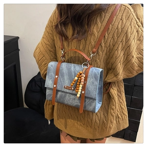 Détail du sac à bandoulière en denim bleu avec garniture en cuir brun et bijou de sac