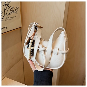 Detailed shot of white crescent shoulder bag featuring stylish wooden bead tassel charm