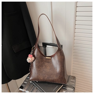 Detail of dark brown leather hobo bag with gold clasp and plush bear charm on suitcase