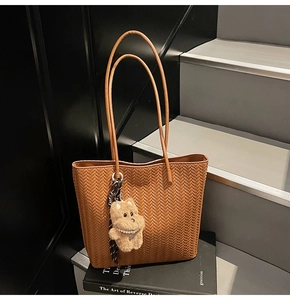 Detailed view of brown woven tote bag with puppy charm and scarf on dark steps