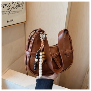Detail of a brown crescent bag featuring leather straps and a colorful wooden bead tassel