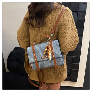 Détail d'un sac bleu vintage avec rivets, étiquette et pompon décoratif en perles