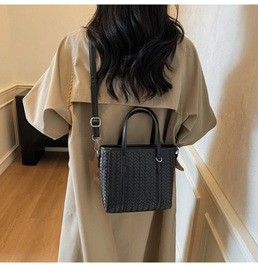 Detail of a black woven bucket bag with adjustable shoulder strap worn with a khaki trench coat