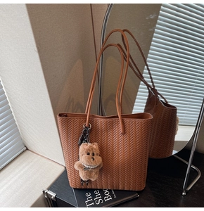 Close-up of brown woven tote bag featuring a plush bear charm and sleek dual straps