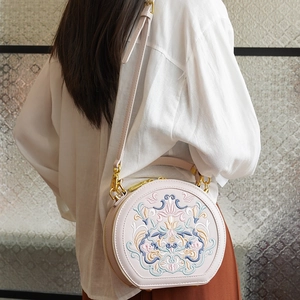 Detail view of round floral embroidery bag with golden hardware and leather strap on a model