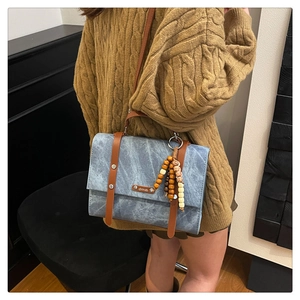 Gros plan du sac messager en toile délavée bleue avec brides en cuir et breloque en perles