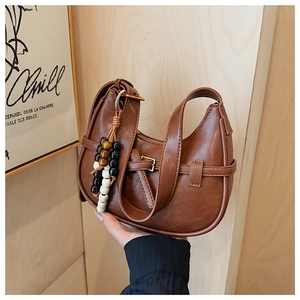 Detail of a brown leather crescent bag featuring a decorative buckle and beaded pendant