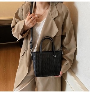 Detail of black woven leather bucket bag styled with a beige trench coat on a model