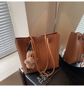 Detail of caramel woven tote bag with V-pattern texture and bear plush pendant charm