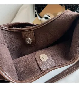 Detail view of the silver magnetic buckle on a coffee brown textured leather bucket bag