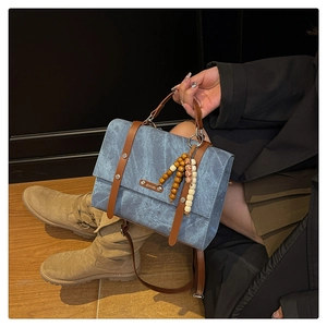 Détail du sac à dos en denim bleu avec lanières en cuir marron et pompon vintage