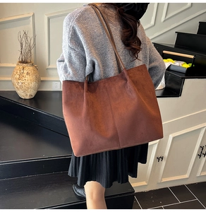 Detail of a large dark brown suede tote bag featuring vertical stitching and a slim strap