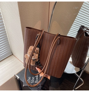 Detail of dark brown woven texture tote bag featuring a cute plush bear charm with pearls