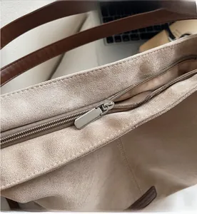 Detailaufnahme von Metallreißverschluss und braunem Lederriemen an beiger Wildledertasche