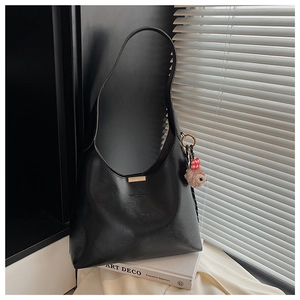 Detail of vintage texture black leather hobo bag with gold bar and plush bear charm