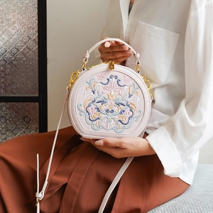 Detailed shot of floral embroidery and gold zipper on round crossbody bag worn by model