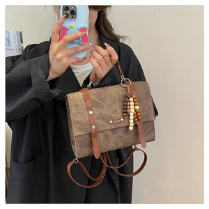 Détail du sac à dos vintage en cuir marron avec breloque perlée et logo métallique