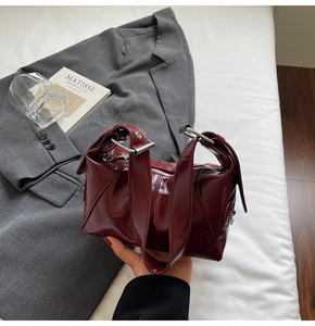 Close-up of deep red glossy leather bag with wide strap and silver hardware accents