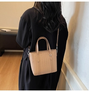 Detail of a beige woven tote bag with silver metal buckles on a wool coat