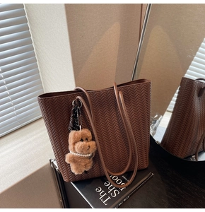 Detailed texture of dark brown woven tote bag featuring a cute teddy bear plush charm