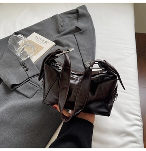 Detailed close-up of dark brown glossy shoulder bag with polished metallic buckles