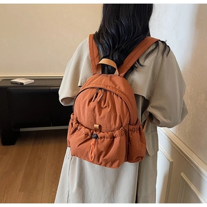 Close-up of burnt orange lightweight nylon backpack showing side drawstring pockets and texture