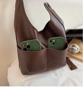 Detail of dark brown leather hobo bag showing two front pockets holding smartphones