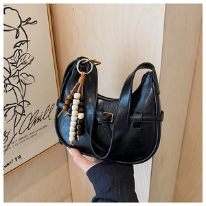 Detail of black PU crescent bag featuring a decorative buckle and wooden bead tassel